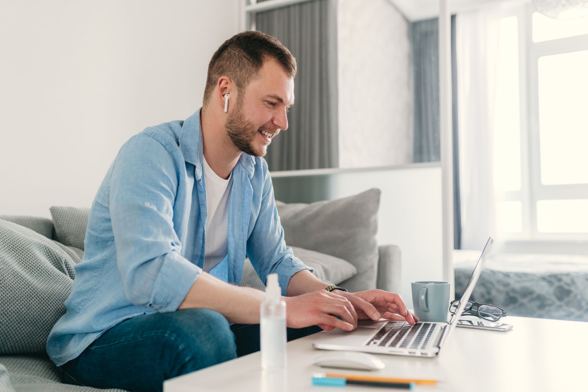 handsome smiling man in shirt sitting relaxed on sofa at home at table working online